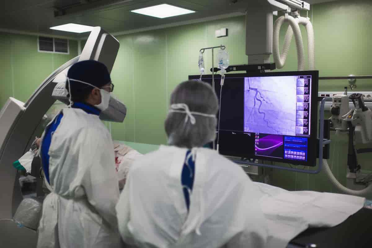 Bildet viser to leger i sterile drakter som ser på en skjerm. På en slags operasjonsbenk foran dem ligger en pasient. 