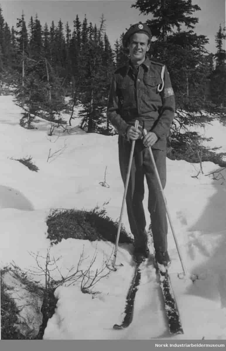 Claus Helberg fotografert stående på ski utenfor Sebrekke radiostasjon våren 1945, i engelsk uniform med hjemmestyrkenes armbind på venstre arm