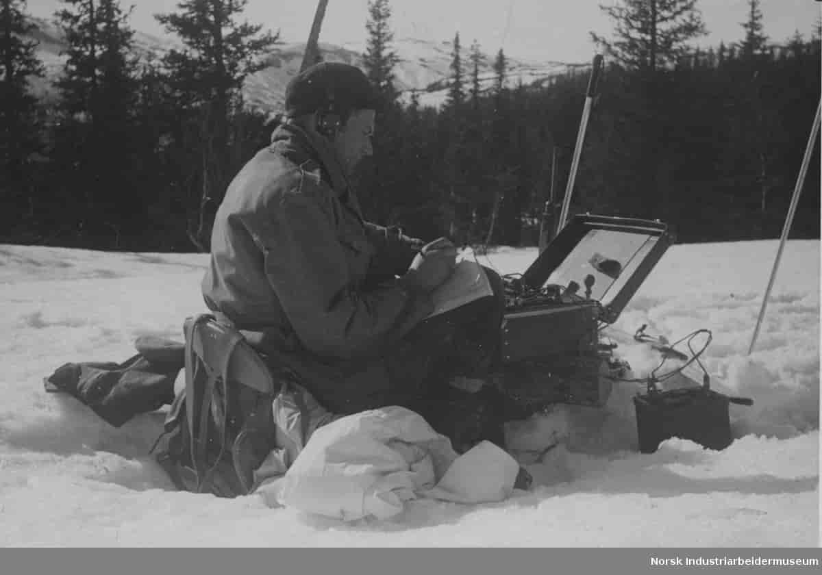 Claus Helberg fotografert sittende i snøen med radiosender/mottager utenfor Sebrekke radiostasjon mars 1945