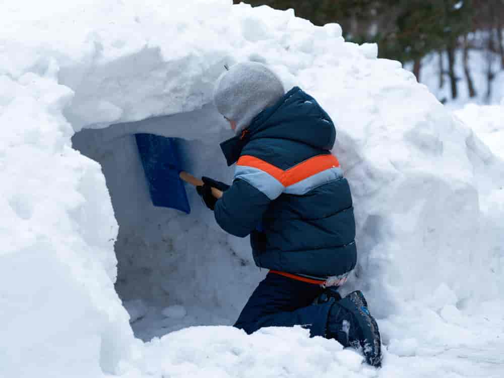 Gutt som graver ut en hule i snøen med spade.