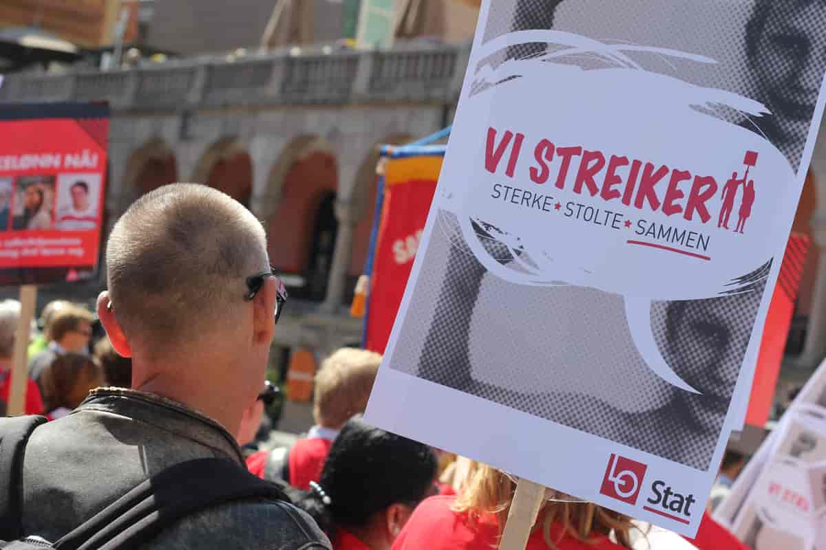 Foto fra Youngstorget i Oslo. Folk står tett i tett og holder plakater. På en av plakatene står det «VI STREIKER. Sterke. Stolte. Sammen.»