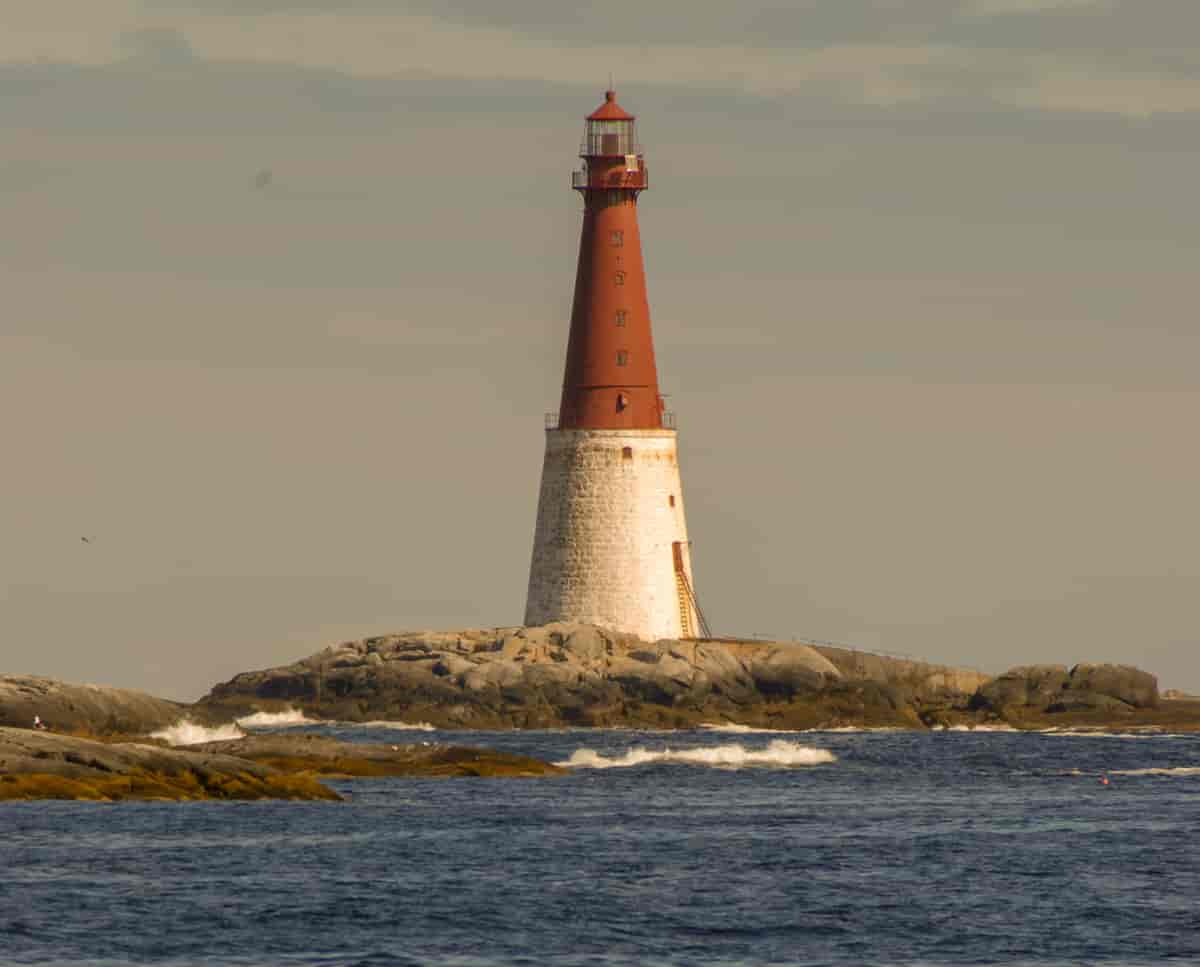Et rødt og hvitt fyrtårn som står på steingrunn som stikker opp fra havet. 