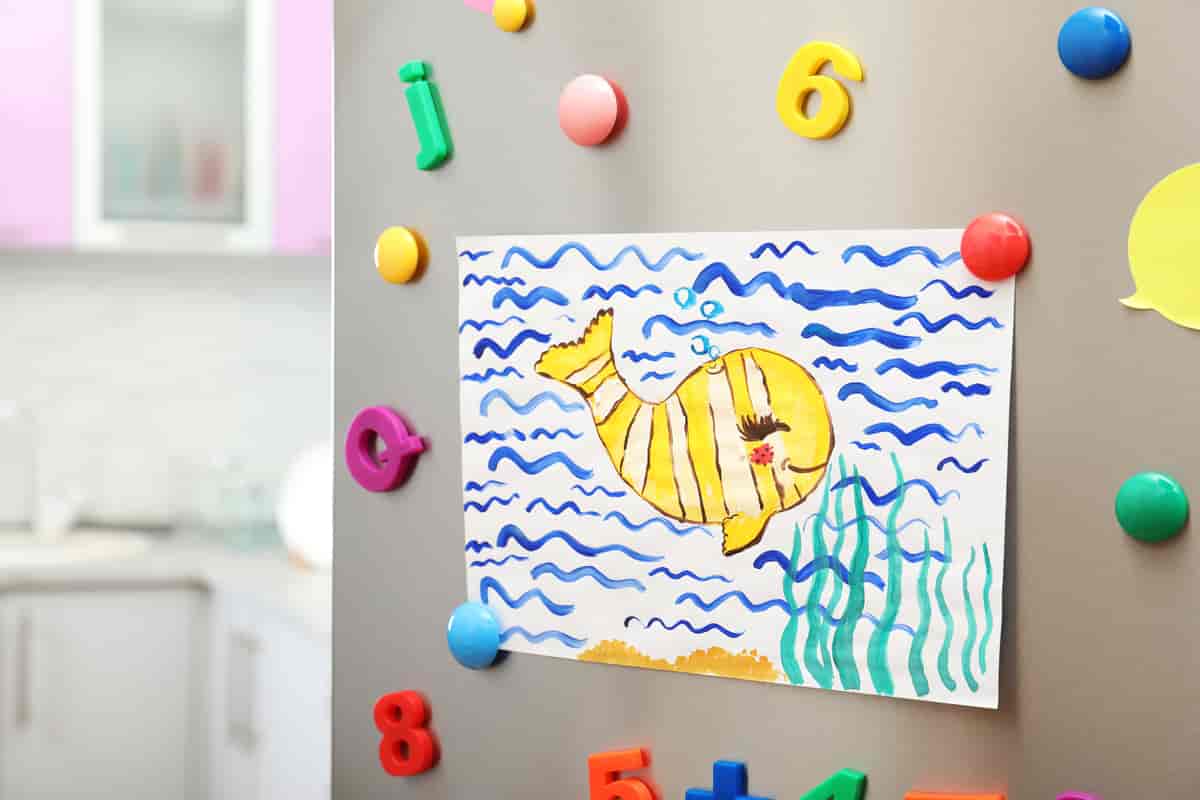 Et kjøleskap med en tegning av en hval som holdes fast med magneter. Rundt tegningen er det magneter formet som bokstaver i forskjellige farger.