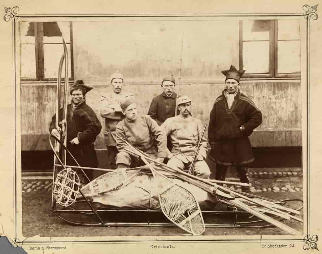 gammelt svart-hvitt foto av fem oppstilte menn. to har på seg samiske kofter