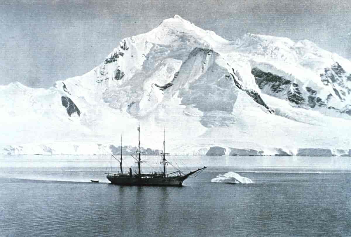 svart-hvitt foto av båt med tre master på sjøen med isfjell i bakgrunnen