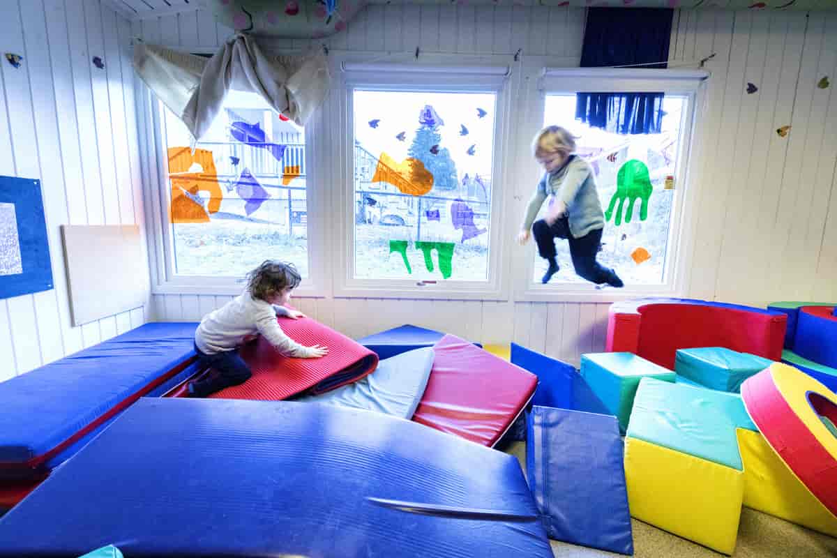 To barn som leker med puter inne i en barnehage.