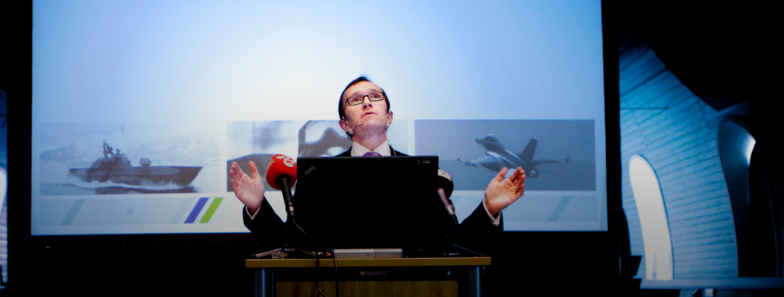 Foto av Barth Eide på et podium foran mikrofoner