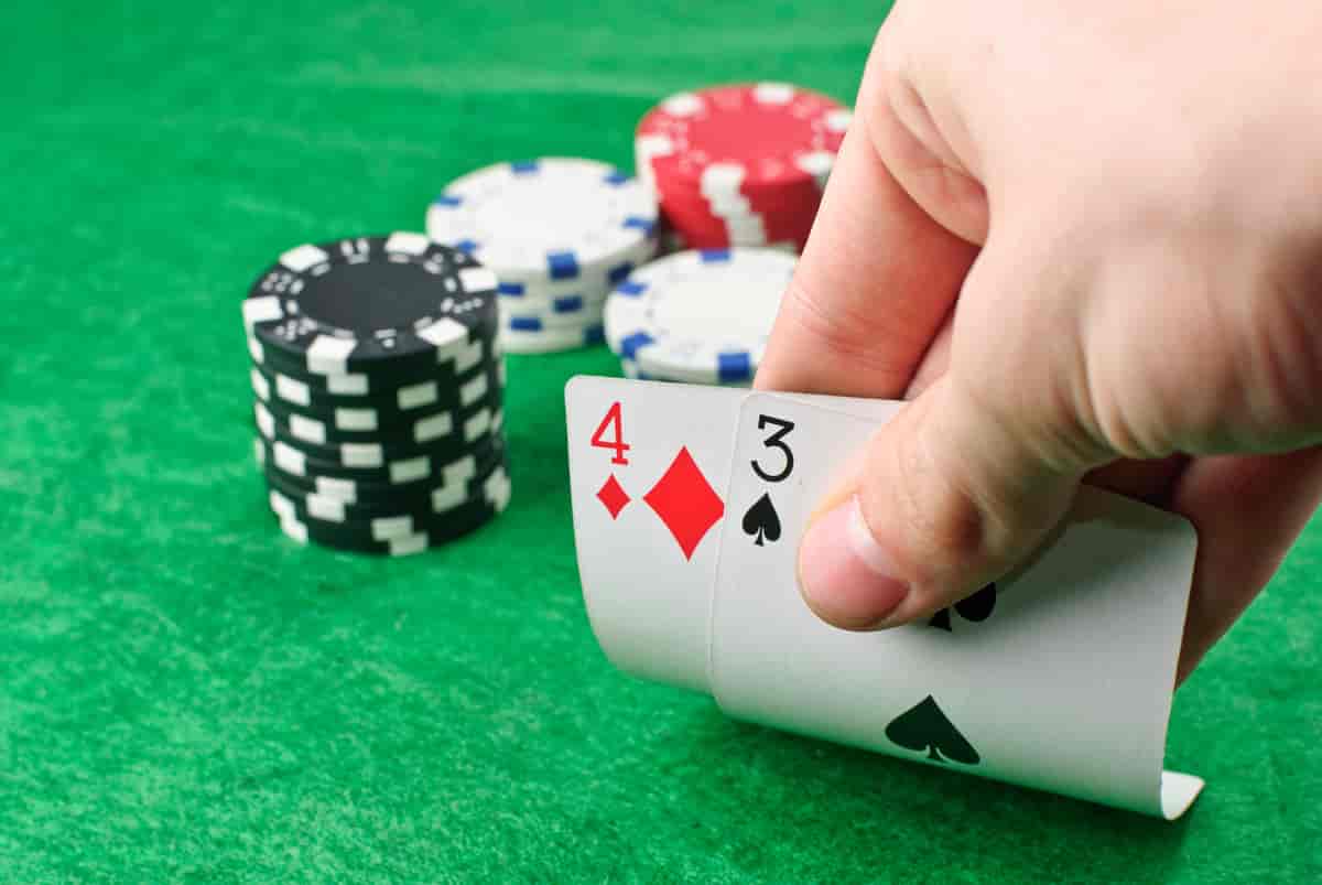 Hånd som holder to spillkort, ett med 4 og ett med 3. I bakgrunnen ligger det spillsjetonger på bordet.