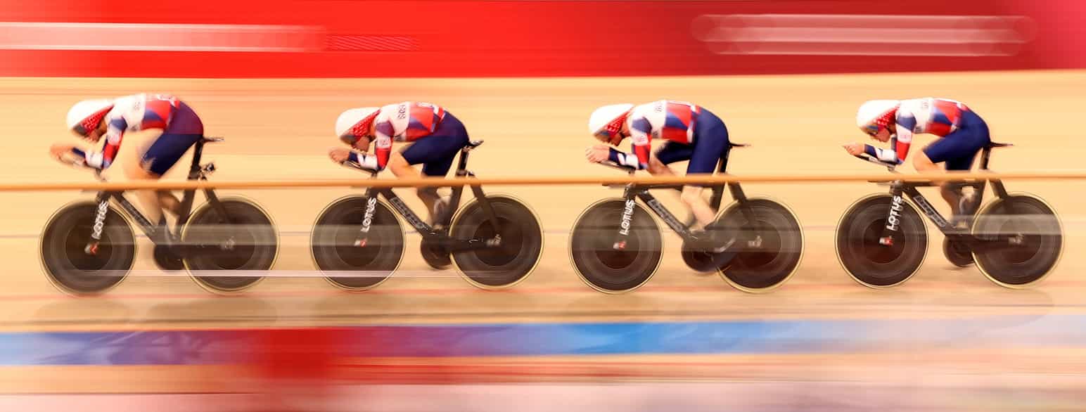 Foto av fire syklister i like drakter som sykler etter hverandre på en innendørs sykkelbane. 