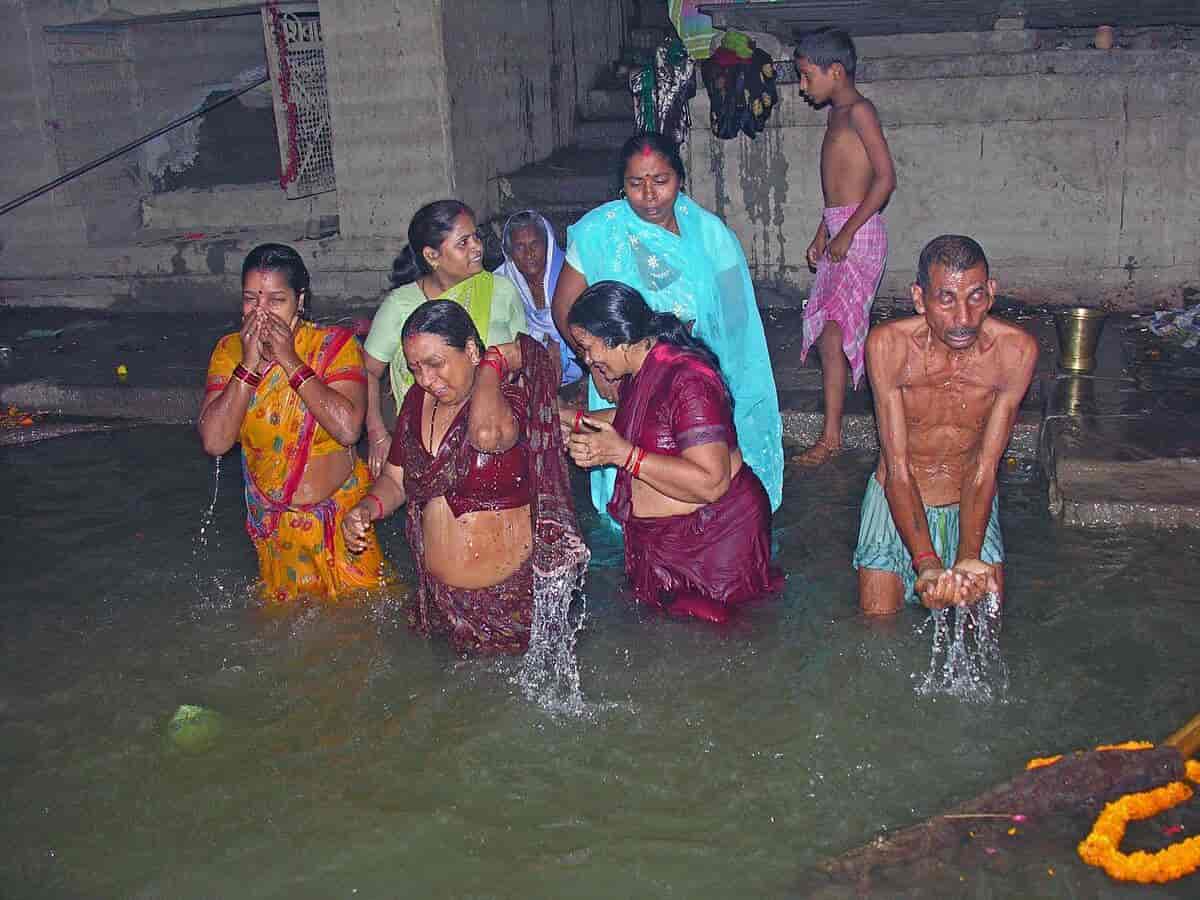 Flere indiske kvinner og menn som vasker seg i en grønn elv.