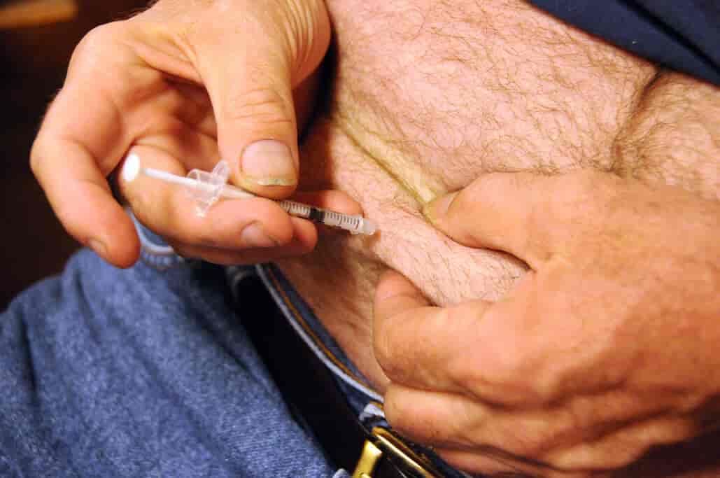 Nærbilde av en mage hvor en mann setter inn insulin med sprøyte. 