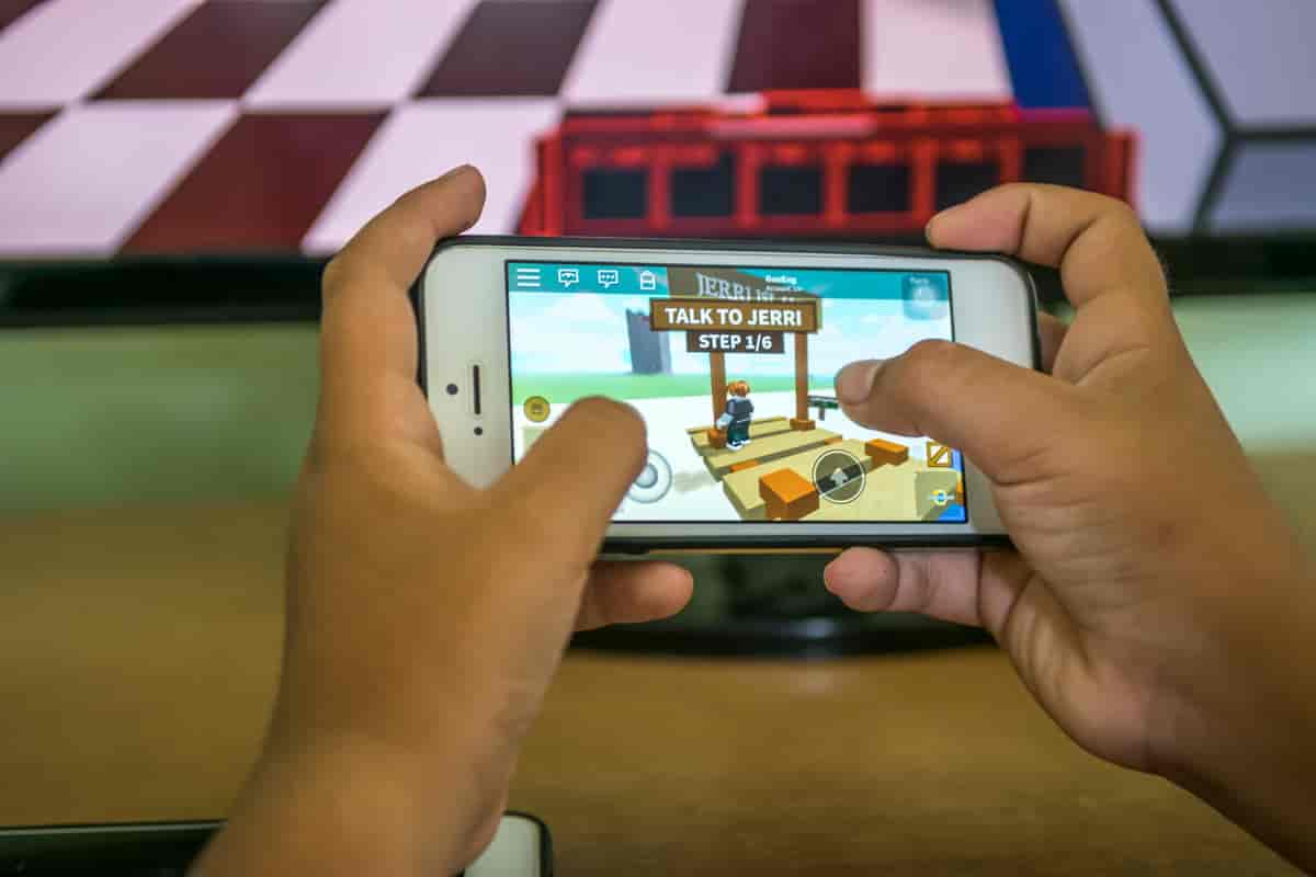 Foto av hendene til en person som holder en smarttelefon med et spill fra Roblox på skjermen.