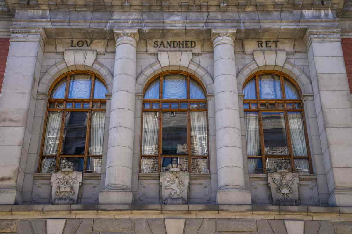 Foto av tre vinduer i en gammel bygning. Over hvert vindu står ett ord. Fra venstre mot høyre står det LOV, SANDHED, RET.