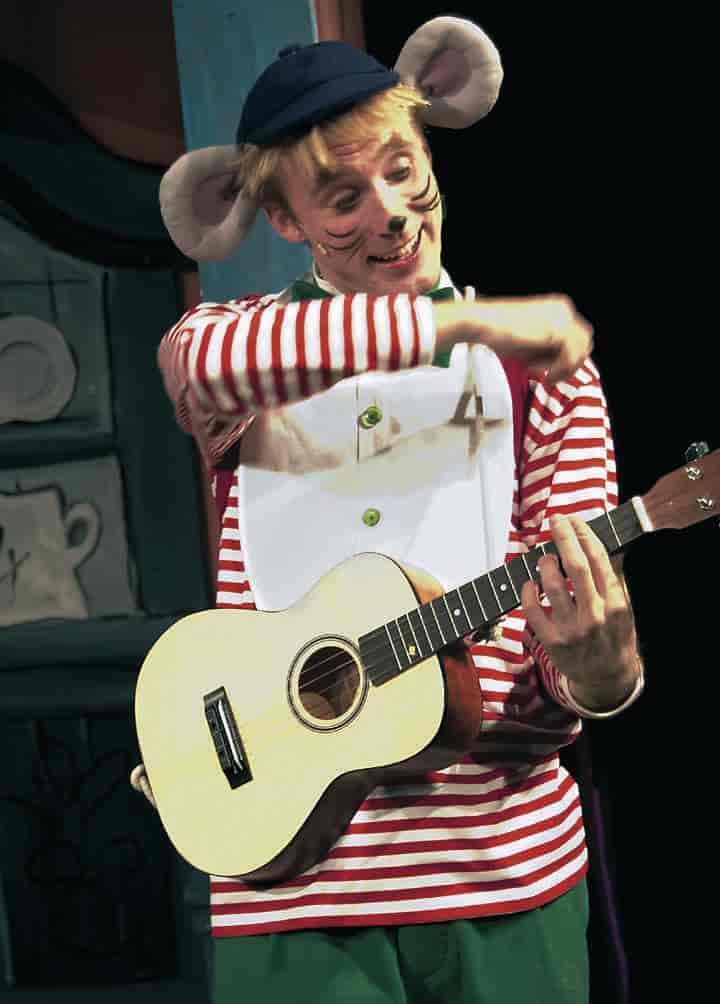 En skuespiller kledd ut som en mus i stripete genser. Han spiller på en liten gitar.