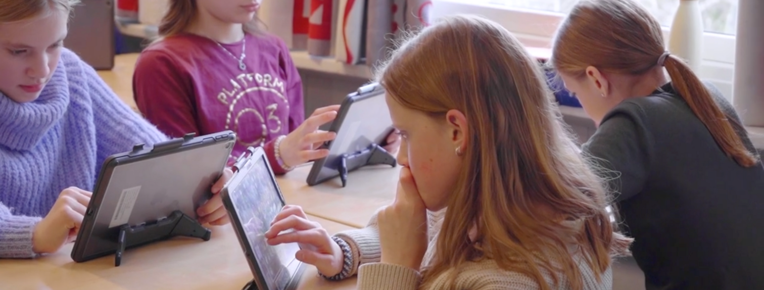 Utsnitt av skjermbilde fra NRK. Fire skoleelever med hvert sitt nettbrett sitter konsentrert og leser.