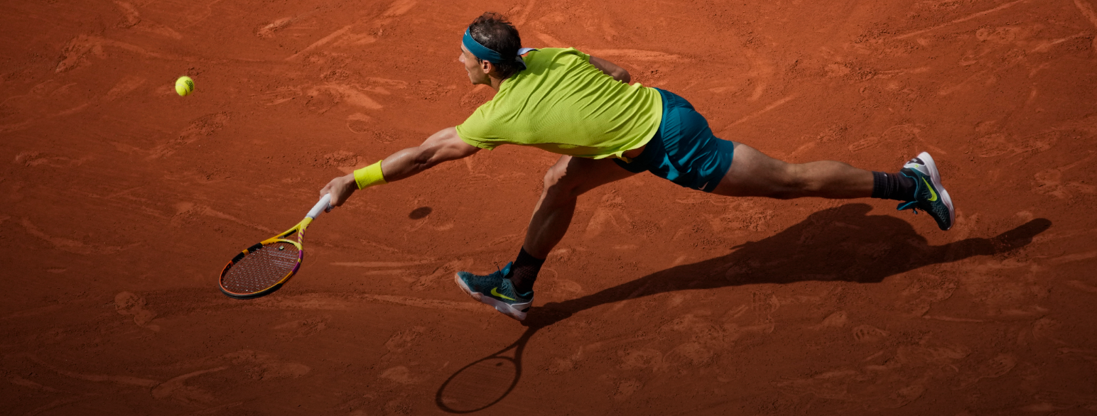 Nadal løper mot en tennisball på grusunderlag, i ferd med å slå til ballen med tennisracketen sin. 