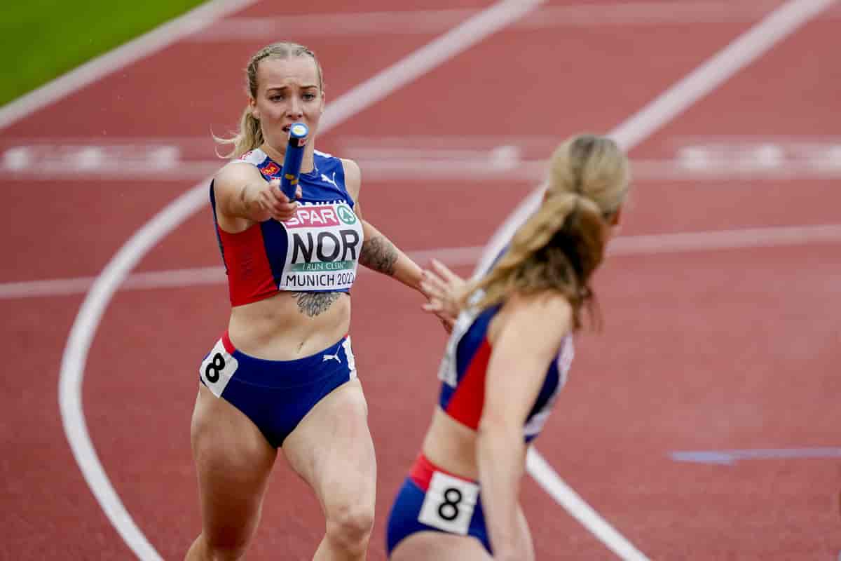 Foto av to norske landslagsløpere. Den ene rekker stafettpinnen mot den andre.