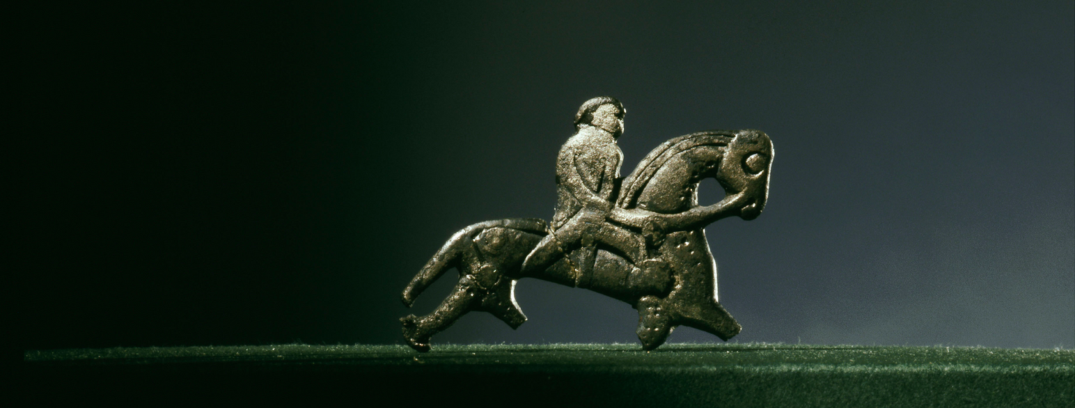 en liten statue i stein av en mann på en hest. Hestefiguren mangler to bein. 