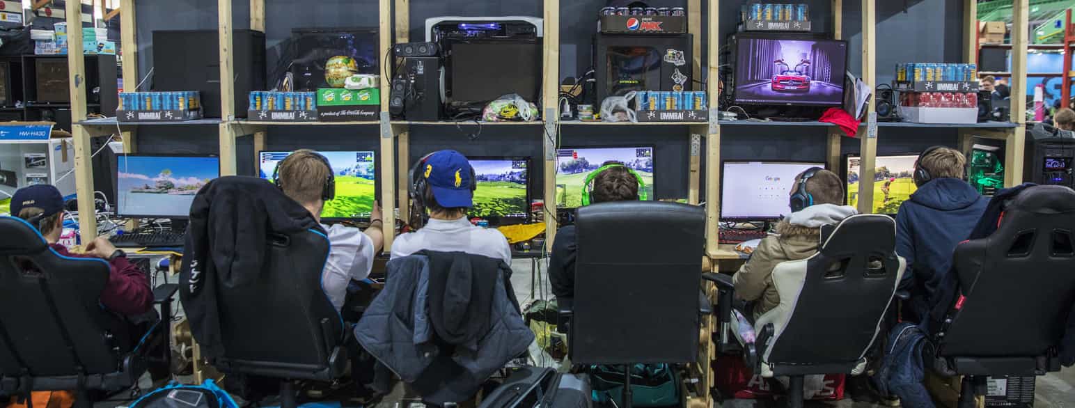 en gruppe ungdommer med ryggen til som spiller spill på hver sin datamaskin