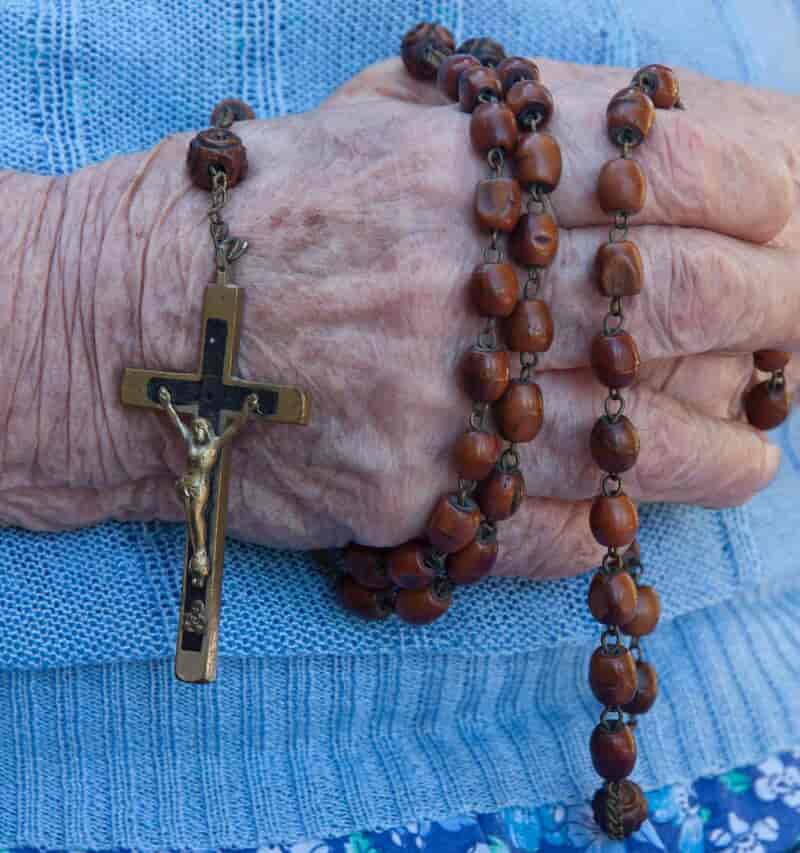 Hånden til en gammel kvinne som holder en bønnekrans med et kors i den ene enden.