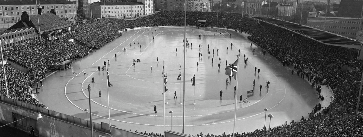 Foto av en fullsatt idrettsarena. Is i misten av arenaen. 