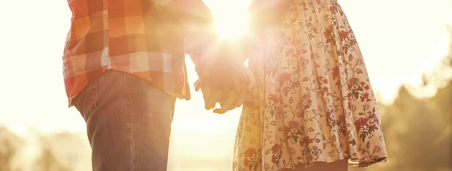 En gutt og en jente holder hender i solnedgang
