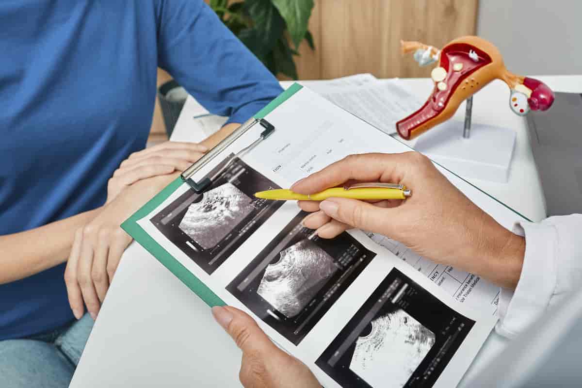 Ein kvinneleg kirurg viser ein pasient bilete frå ei ultralydundersøking. Ho bruker ein anatomisk modell av ei livmor som hjelpemiddel når ho forklarer dette til pasienten.