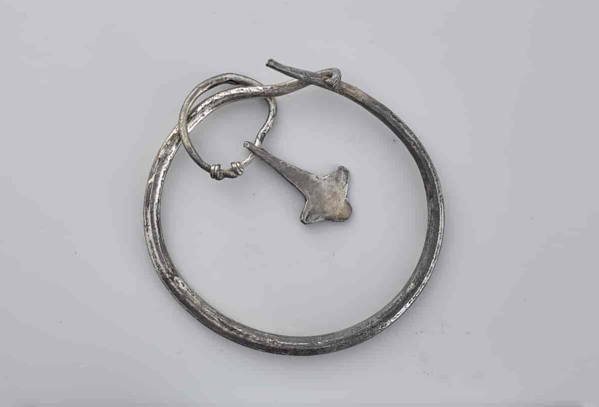 En armring av et slags metall. En litt mindre ring er festet i armringen. Til den minste ringen er det festet en figur med form som en hammer.