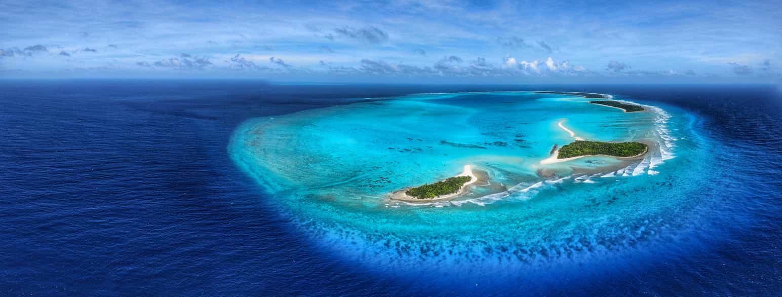 Luftfoto av en atoll med fire små øyer. Inne i atollen er vannet turkist, utenfor er det blått.