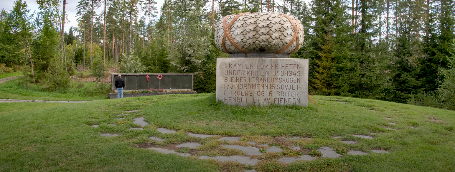 Steinskulptur i forgrunnen, men en minnetavle bak med navnene på de henrettede.