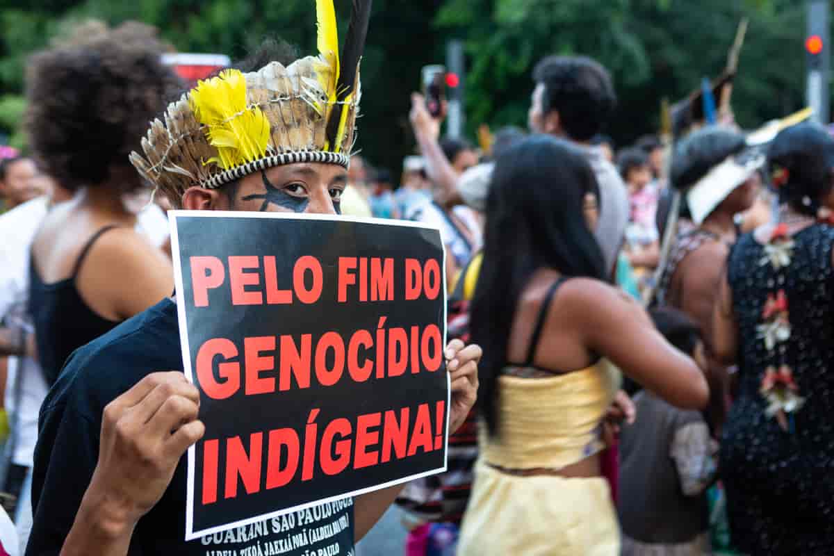 En mann holder en plakat som sier «For en slutt på folkemordet på urfolk»