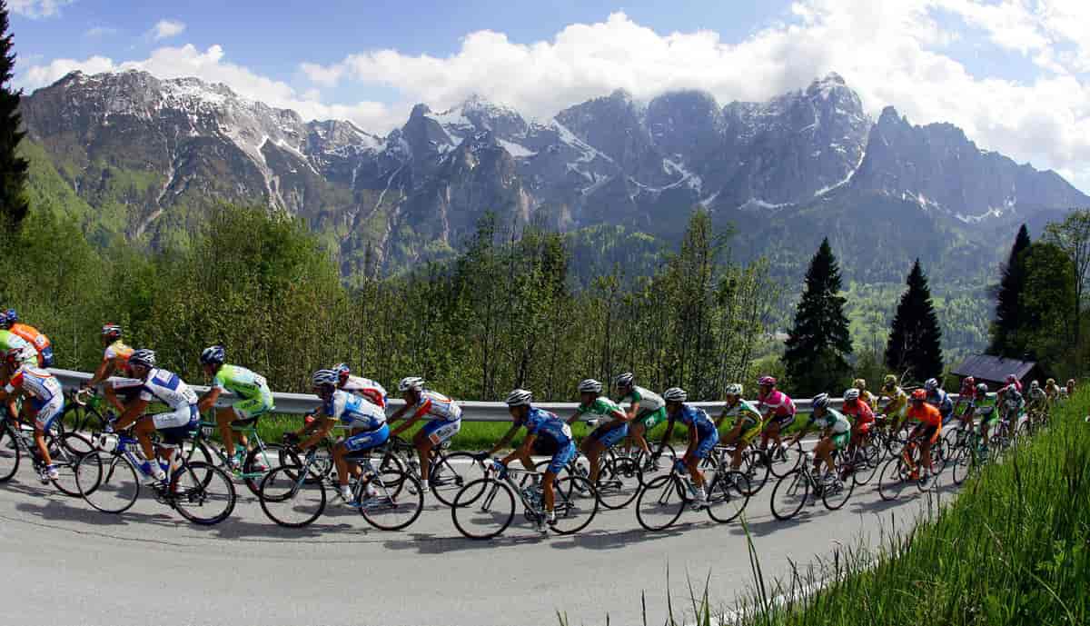 Syklister på rekke sykler opp en lang bakke i fjellene. 