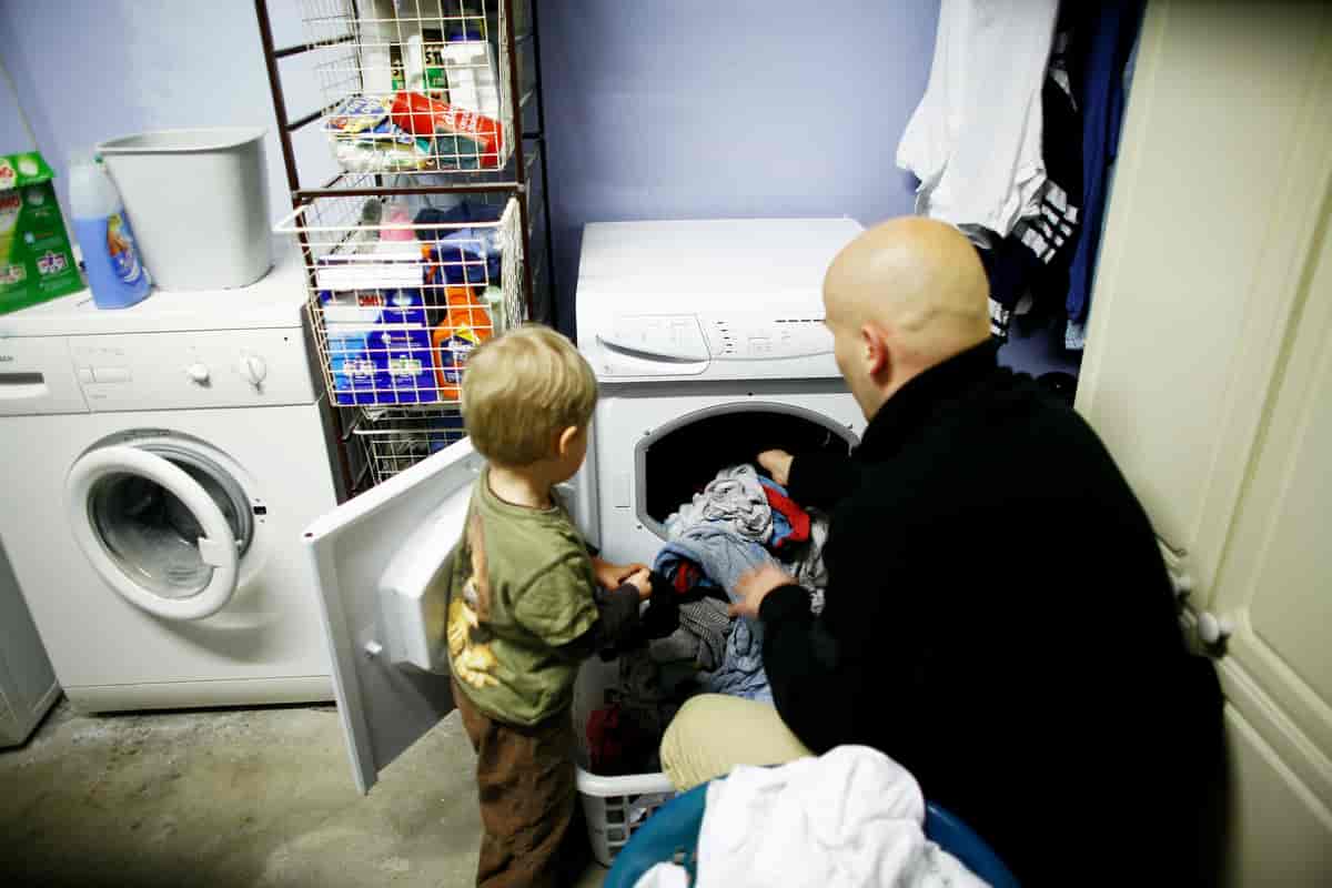 Fotografi av en mann og et barn som putter klær inn i en vaskemaskin. 